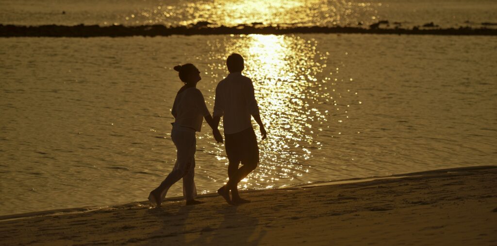 pár se prochází po pláži při západu slunce