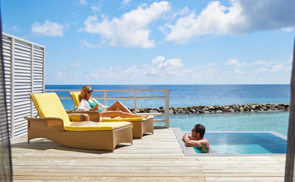 žena na lehátku na terase vodní vily a muž v bazénu